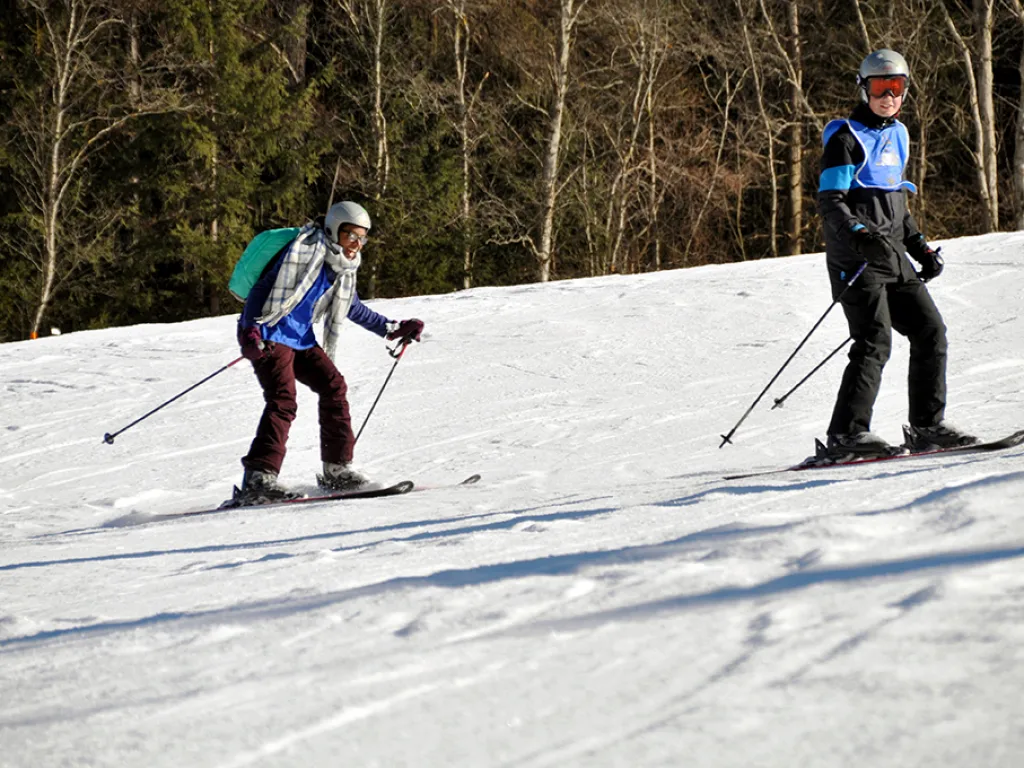 Zwei Skifahrende auf der Piste am Waldrand.